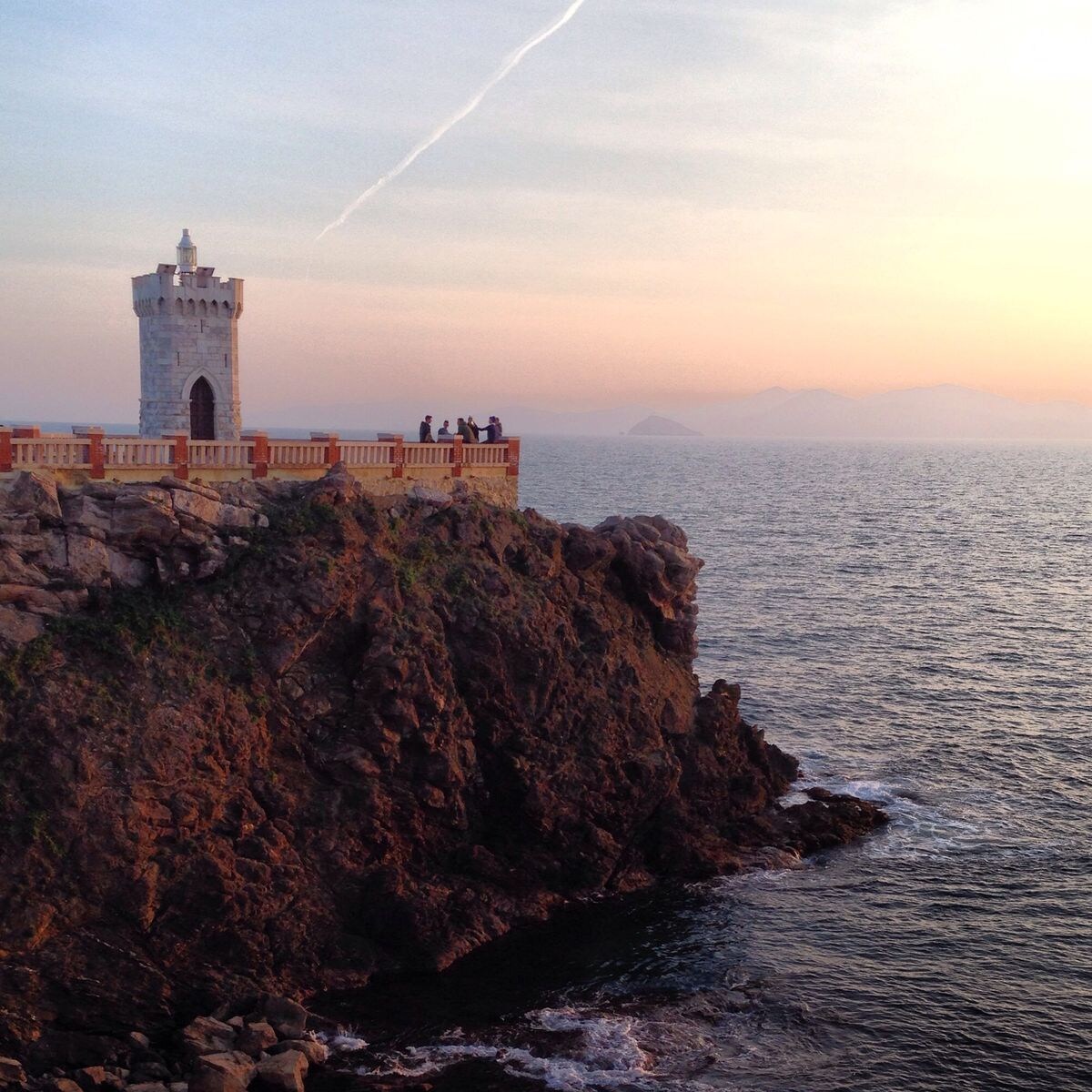 Il faro di Piazza Bovio sulla scogliera al tramonto, con il mare e l'Arcipelago Toscano sullo sfondo