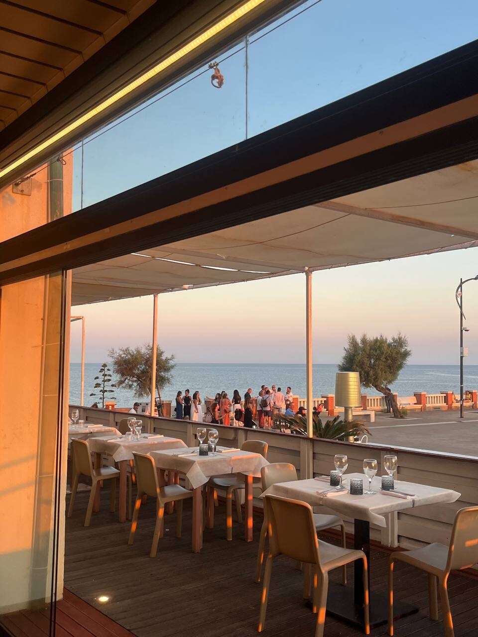 Tavoli apparecchiati sulla terrazza de La Rocchetta nella luce dorata della sera, con il mare sullo sfondo